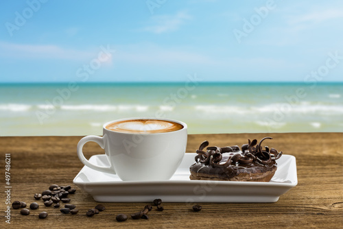Donut chocolate and latte coffee on wooden table with sea background