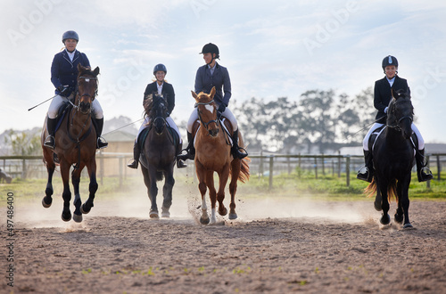 Theyre neck-and-neck. Full length shot of a group of attractive young female jockeys riding their horses out on the farm. © Nina L/peopleimages.com