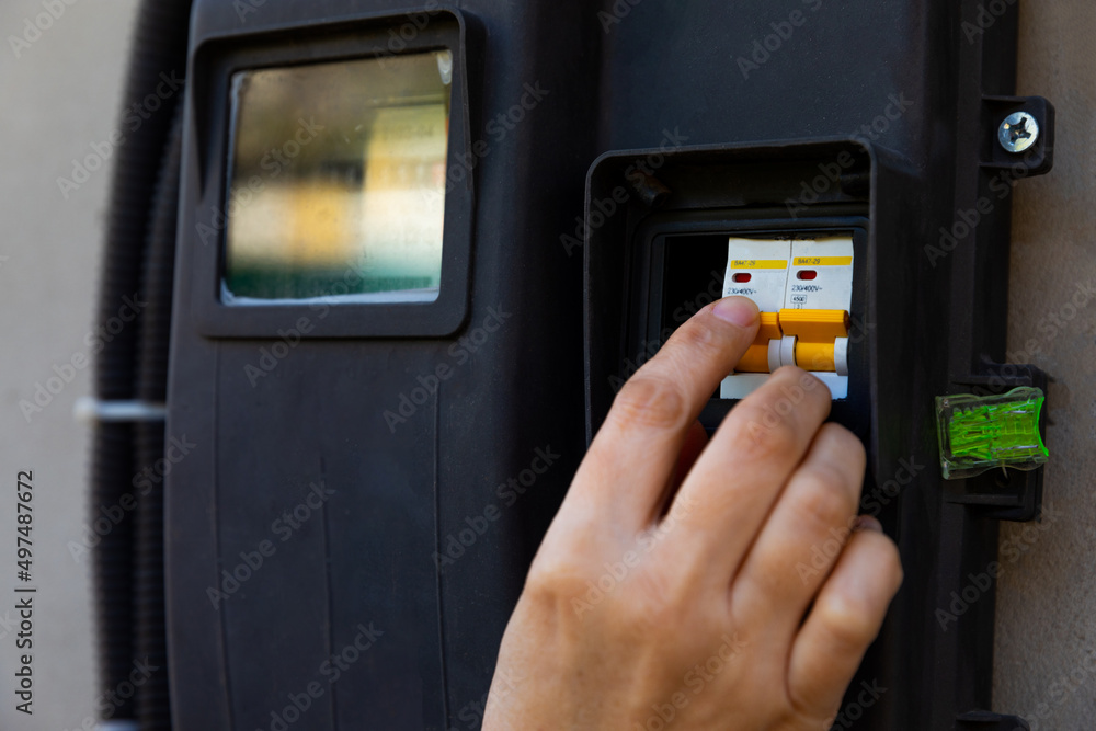 Electric meter. A woman's hand turns on a toggle switch on an electric ...
