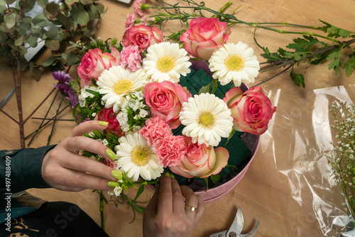 Top view of the hands of a young female florist creating a beautiful composition of delicate pink roses and white daisies on the table