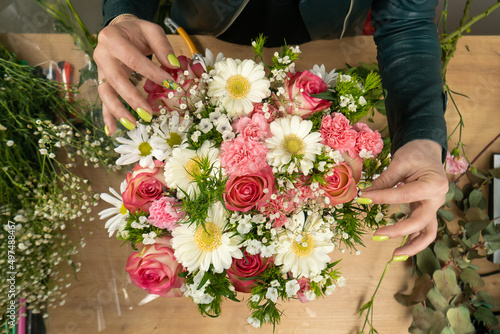 Top view of the hands of a young female florist creating a beautiful composition of delicate pink roses  carnations and white daisies on the table