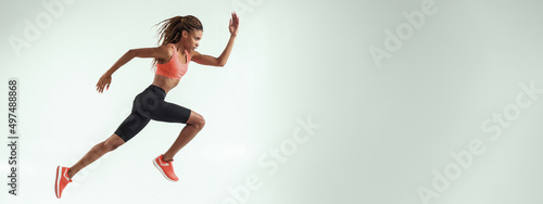 Never give up. Full length of young african woman with perfect body in sports clothing jumping in studio against grey background