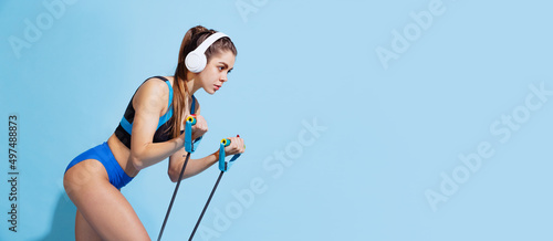 One young beautiful sportive girl in sports uniform training with sports equipment isolated on blue studio background. Sport, action, fitness, youth concept.
