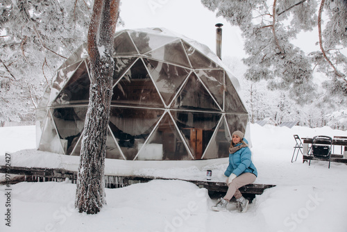 Obraz na płótnie A woman sits and enjoys the view next to a dome tent in glamping in the winter forest w salonie