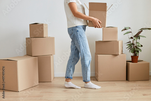 Image of faceless anonymous unknown woman wearing jeans and white shirt holding cardboard box in hands, unpacking parcels during relocating to another flat.