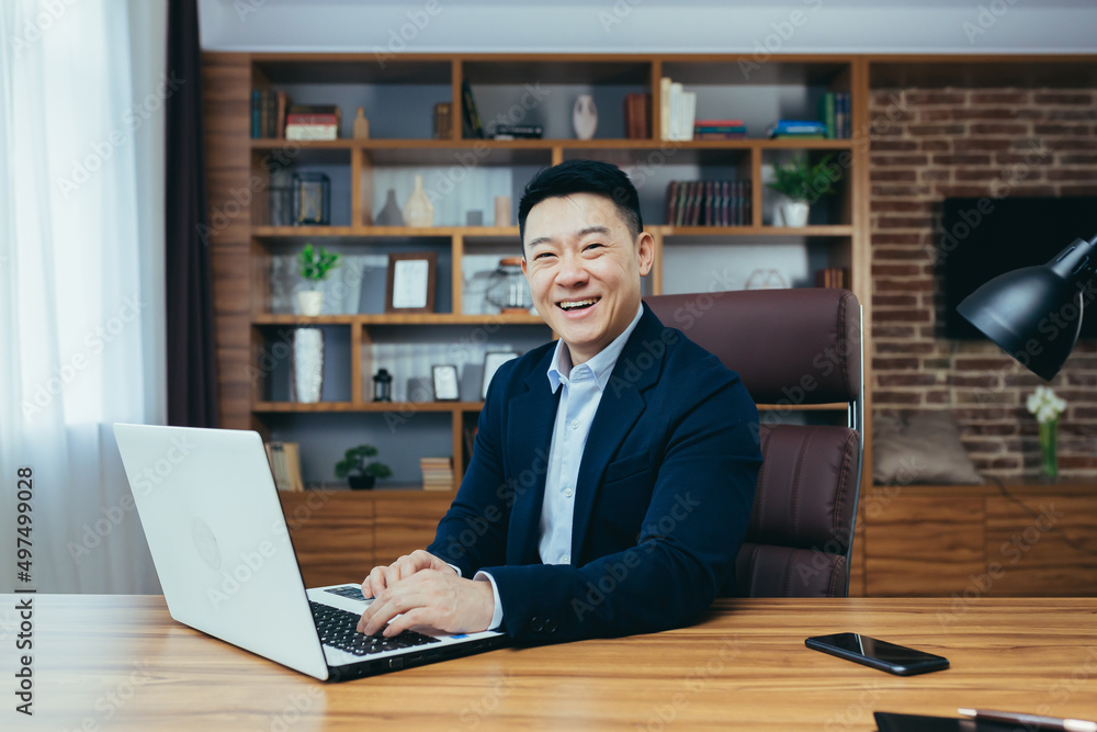 Portrait of a successful Asian businessman in a classic office working on a laptop, smiling Portrait of a successful Asian businessman in a classic office working on a laptop, smiling