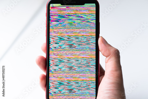 A hand holding smartphone, mobile phone closeup. Glitches, distorted, corrupted image with colorful lines on the phone. Color channels effect.
