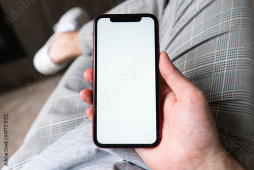 Young man hands holding mobile smart phone with mockup white blank display, empty screen at home. Shopping, delivery apps, social media applications ads, close up view.