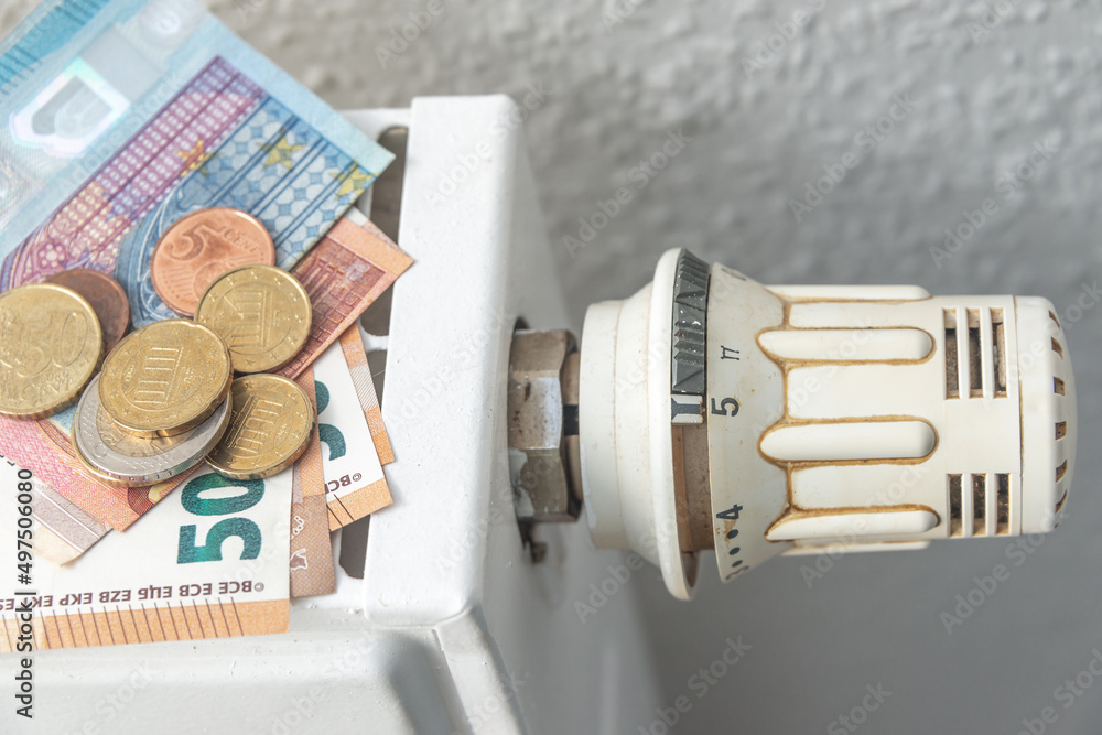 House heating battery with maximum heating power setting dial and a pile of money banknotes and coins in euro. Concept of energy consumption, energy crisis in households. House heating battery with maximum heating power setting dial and a pile of money banknotes and coins in euro. Concept of energy consumption, energy crisis in households.