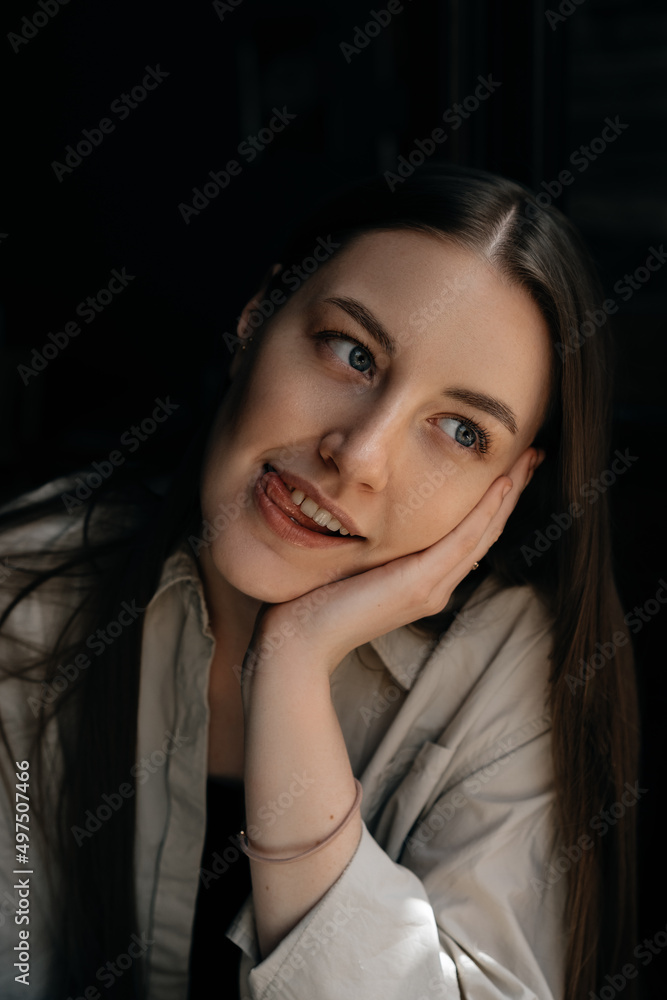 Portrait of a young European girl with long dark hair in a beige shirt with her tongue sticking out looks away. She feels happy.
Portrait of a young European girl with long dark hair in a beige shirt with her tongue sticking out looks away. She feels happy.