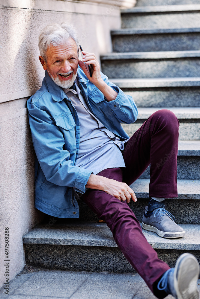 A happy laughing senior man is sitting on the stairs outdoors and flirting on the phone. A happy laughing senior man is sitting on the stairs outdoors and flirting on the phone.