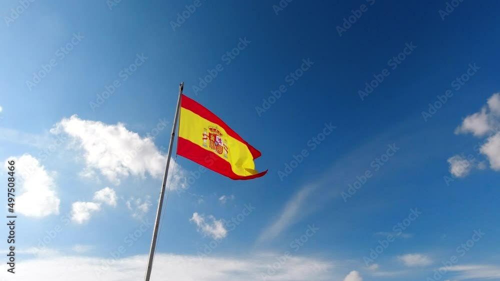 National flag of Spain waving in slow motion against cloudy blue sky National flag of Spain waving in slow motion against cloudy blue sky