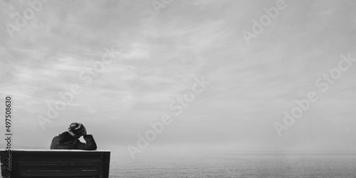 Unhappy single woman sitting on bench, looking at distant sea or seascape horizon. Lonely young woman missing someone concept idea. Time to go, say goodbye or good bye. Black and white photography.