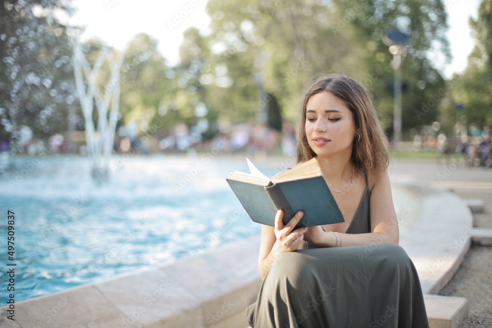 young woman sitting on the edge of a fountain in a park reads a book young woman sitting on the edge of a fountain in a park reads a book