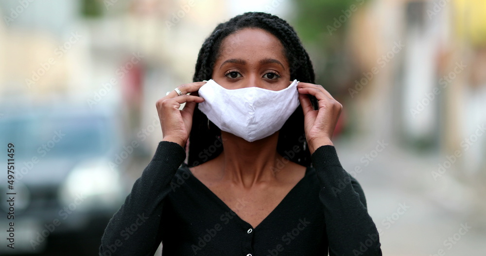 African girl putting covid-19 face mask prevention outside in street staring camera African girl putting covid-19 face mask prevention outside in street staring camera