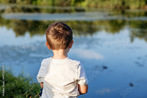 Lake child back to camera. Childhood in the village. Little boy in a T-shirt on background of the lake