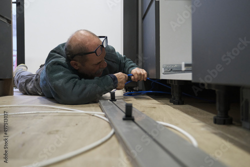 Mature technician installing plastic tubes to connect water filter to an american refrigerator in kitchen. photo
