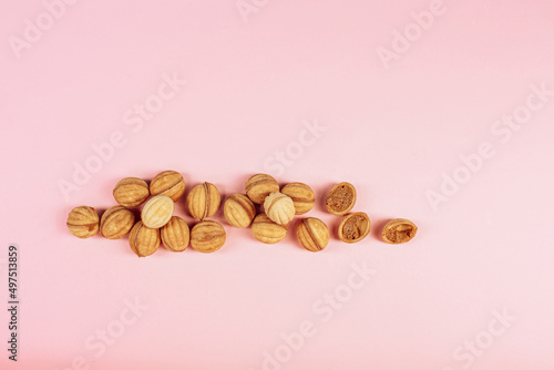 delicious walnut shaped shortbread sandwich cookies filled with sweet condensed milk and chopped pistachio nuts on brown clay dish. on pink background, view from above, close-up