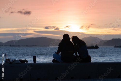 two stylish girl or lady chat at seaside during sunset in evening. Back light view