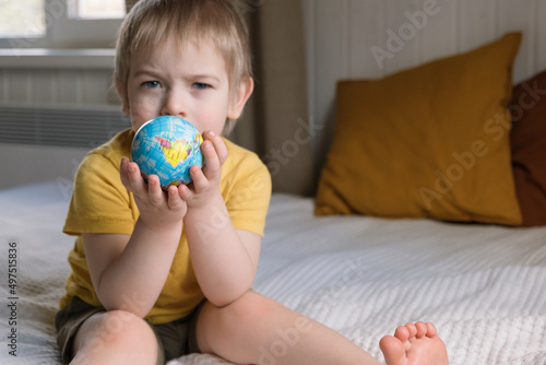Child boy with blonde hair hugging the earth globe, save the earth concept. 3 years old kid holding a toy globe model. Baby toddler. Early, age children education development