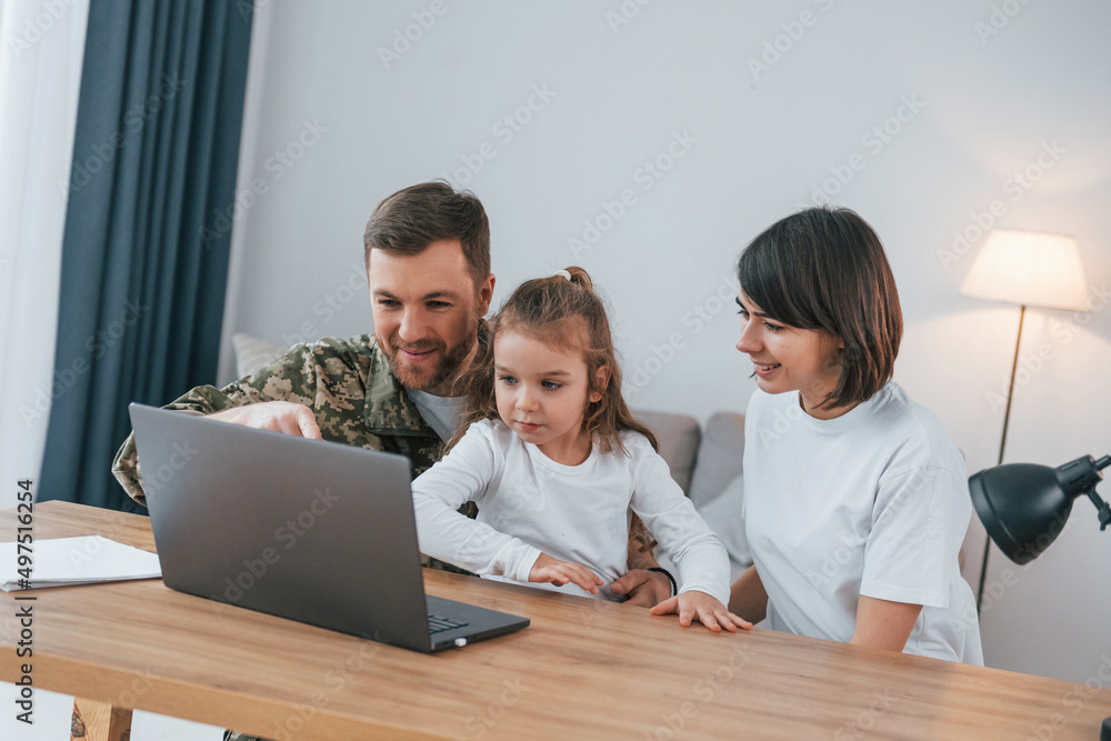 Talking by using laptop. Soldier in uniform is at home with his wife and daughter Talking by using laptop. Soldier in uniform is at home with his wife and daughter