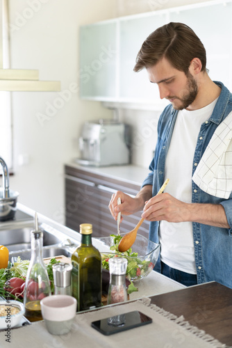 Young man preparing vegetable salad in the kitchen. Happy man making healthy meal