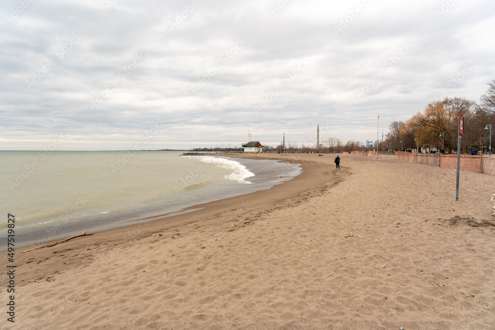 A lone figure walks on Toronto's Kew Beach on a spring evening with the city skyline in the far back ground.  Room for text.