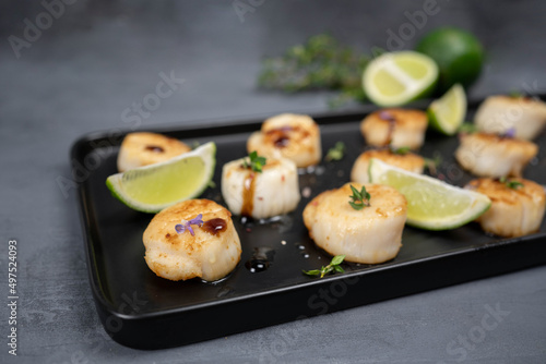 Fried scallops with butter lemon spicy sauce on black plate over old dark stone background.