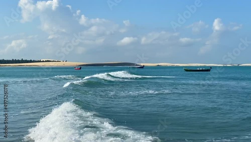 Waves going through at the Jericoacoara beach with boats anchored and the sunset dune in the background