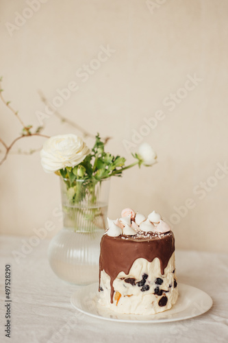 Easter cake decorated with chocolate and marshmallows. Easter cake is on the table, also on the table is a vase of flowers. The holiday table. © Oleg