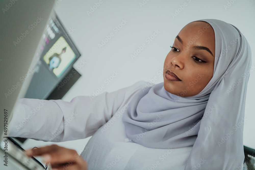 Young Afro-American modern Muslim businesswoman wearing a scarf in a creative bright office workplace with a big screen. Young Afro-American modern Muslim businesswoman wearing a scarf in a creative bright office workplace with a big screen.