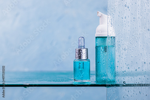 Lotion, oil or serum in blue dropper bottle behand of glass with water drops with copy space. Spa product. Organic, bio, natural cosmetic. Beauty, skincare concept.