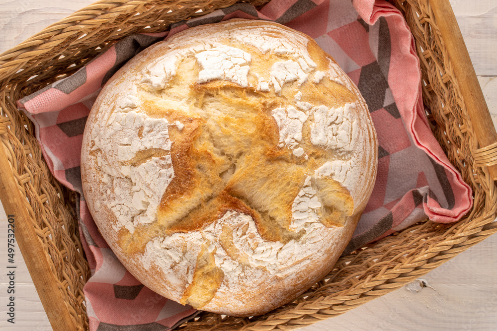 One loaf of fresh fragrant white wheat bread in a basket on a wooden table, macro, top view.