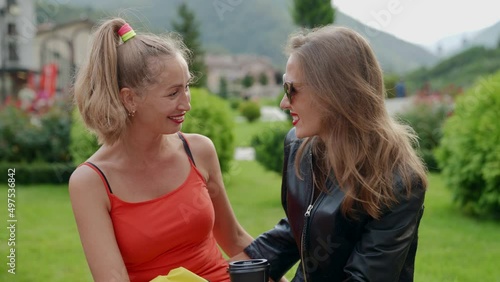 portrait of two girlfriends with bright lipstick on the background of mountains. blondes look at each other and laugh photo