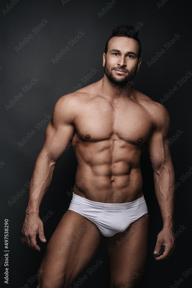 Handsome man in white underwear standing in studio at dark grey background