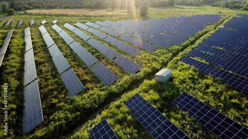 Aerial Top view on Solar Power Station in Green Field on Sunny day. Drone fly over Solar Farm. Lot of Solar Panels Stand in Row for Power Production. Renewable green energy