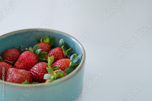 Red fresh strawberries with green leaves in plate on gray background. Side view  copy space