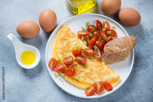 Omelet with fresh sliced cherry tomatoes served on a white plate, studio shot on a light-blue stone background