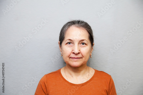 Portrait of 60-year-old woman on gray background.