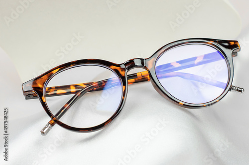 Leopard-colored glasses on a white silk fabric, close-up
