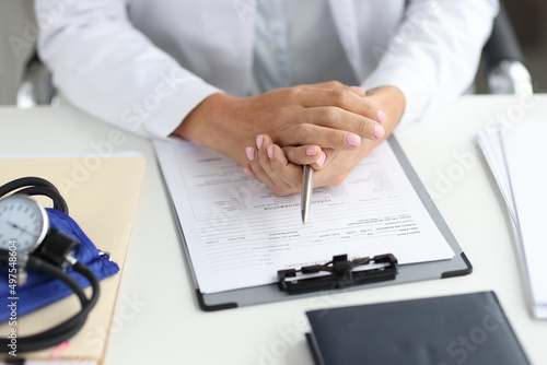 Doctor holds pen and medical record at workplace closeup