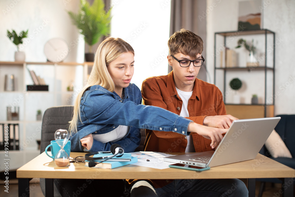 Students, man and woman in casual outfit using laptop during working together. Young business partners cooperating at bright office or working online from home Students, man and woman in casual outfit using laptop during working together. Young business partners cooperating at bright office or working online from home