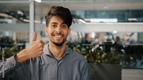 Happy hispanic employee arab man leader winner approve looking at camera showing thumb up agreement sign everything fine success gesture body language in office recommend good choice close-up portrait