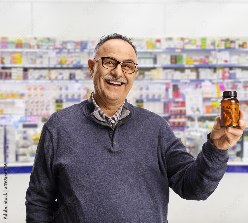 Mature man holding a bottle of medications and smiling inside a pharmacy Mature man holding a bottle of medications and smiling inside a pharmacy