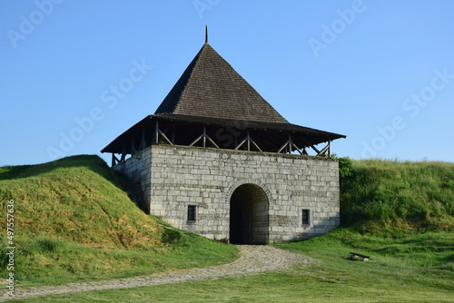 Large tower of a medieval stone fortress with an arched entrance and earthen ramparts on the sides