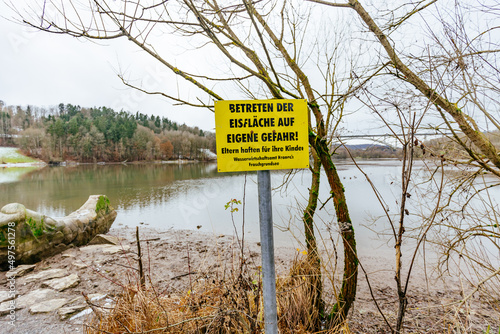 Fotografie Beautiful shot of a yellow sign entering the ice at your own risk Froschgrundsee