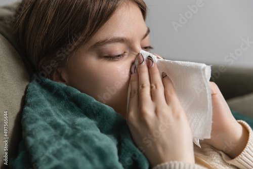 a sick girl blows her nose with a cold in a paper napkin lying on the couch