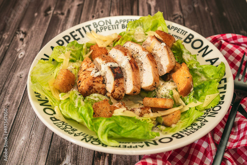 Caesar salad with thinly sliced chicken breast and traditional aioli on a plate that says bon apetite on a rustic table. Natural alimentation, healty food. photo