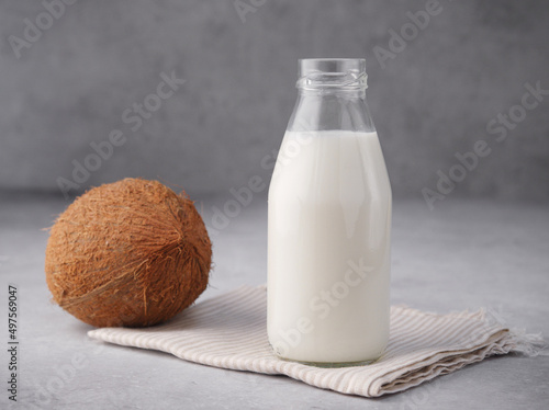 Coconut vegan milk is non dairy products in a bottle with a place to copy on a gray concrete background. Glass bottle of milk or yogurt with coconut chips aside. Concept of healthy eating. Close up.