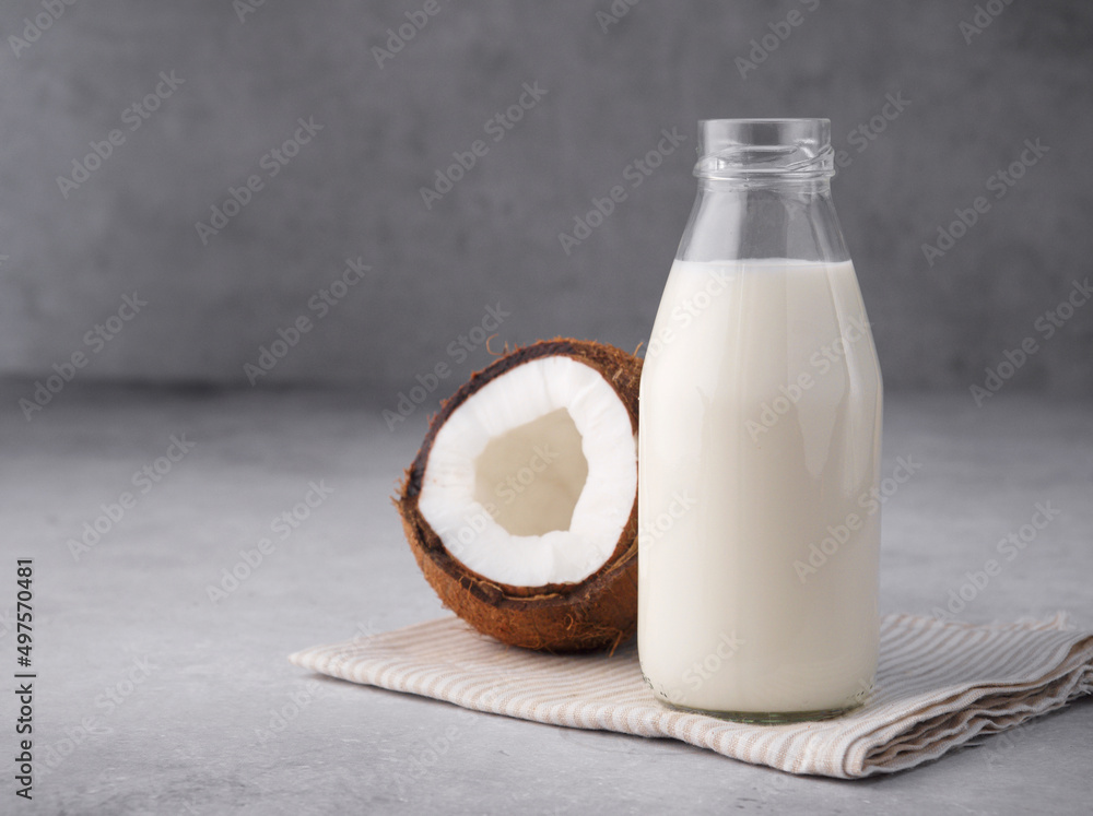 Coconut vegan milk is non dairy products in a bottle with a place to copy on a gray concrete background. Glass bottle of milk or yogurt with coconut chips aside. Concept of healthy eating. Close up. Coconut vegan milk is non dairy products in a bottle with a place to copy on a gray concrete background. Glass bottle of milk or yogurt with coconut chips aside. Concept of healthy eating. Close up.